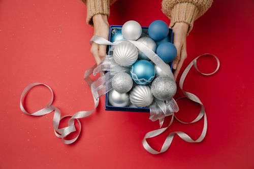 Free From above of anonymous female holding small gift box with blue silver and pearl baubles and thin ribbon Stock Photo
