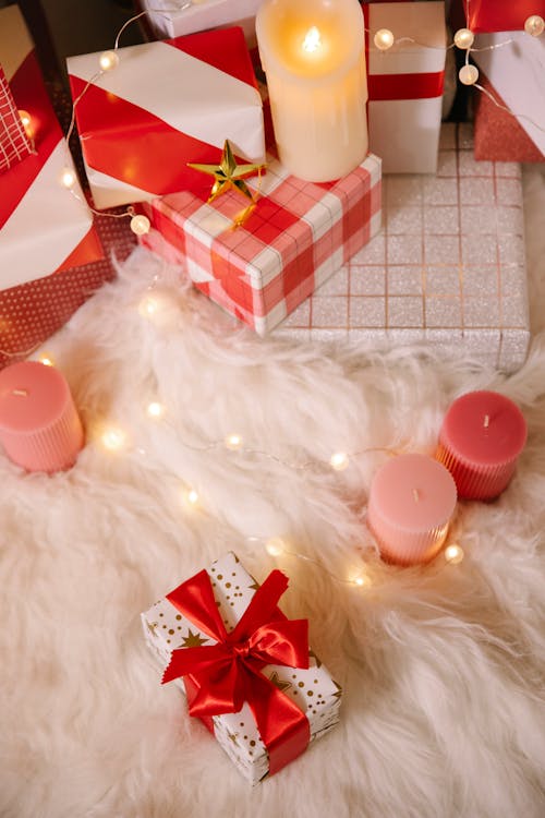 High angle of Christmas composition with wrapped boxes with presents candles and lighted garland on  white fur