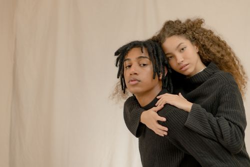 Free Young couple in black sweaters sharing a heartfelt moment against a beige backdrop. Stock Photo