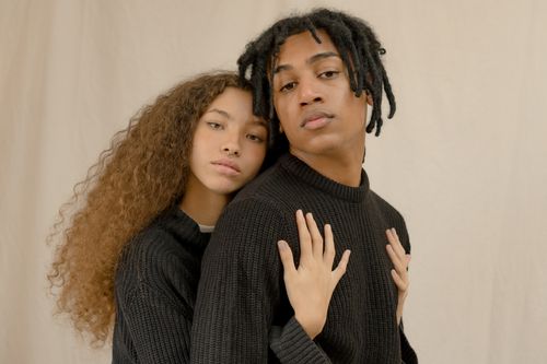 Free A couple in matching sweaters embraces with a soft, warm expression against a beige background. Stock Photo