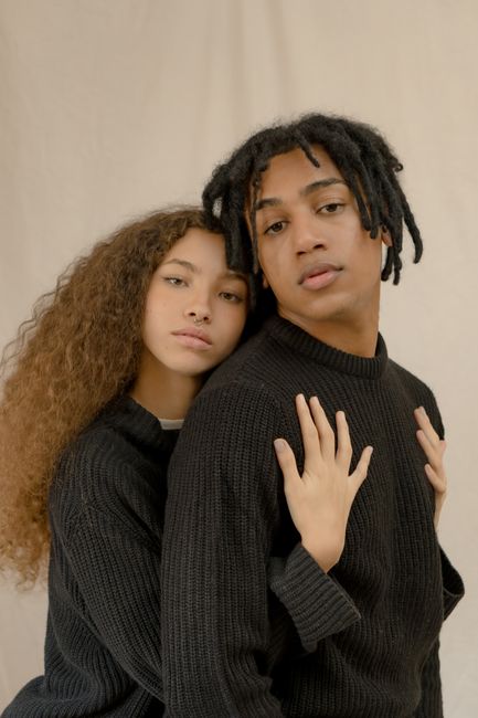 Portrait of a couple in black sweaters embracing against a beige background, showcasing a romantic bond.