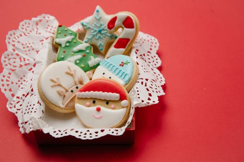 High angle of small box with Christmas biscuits decorated with colourful icing on white doily