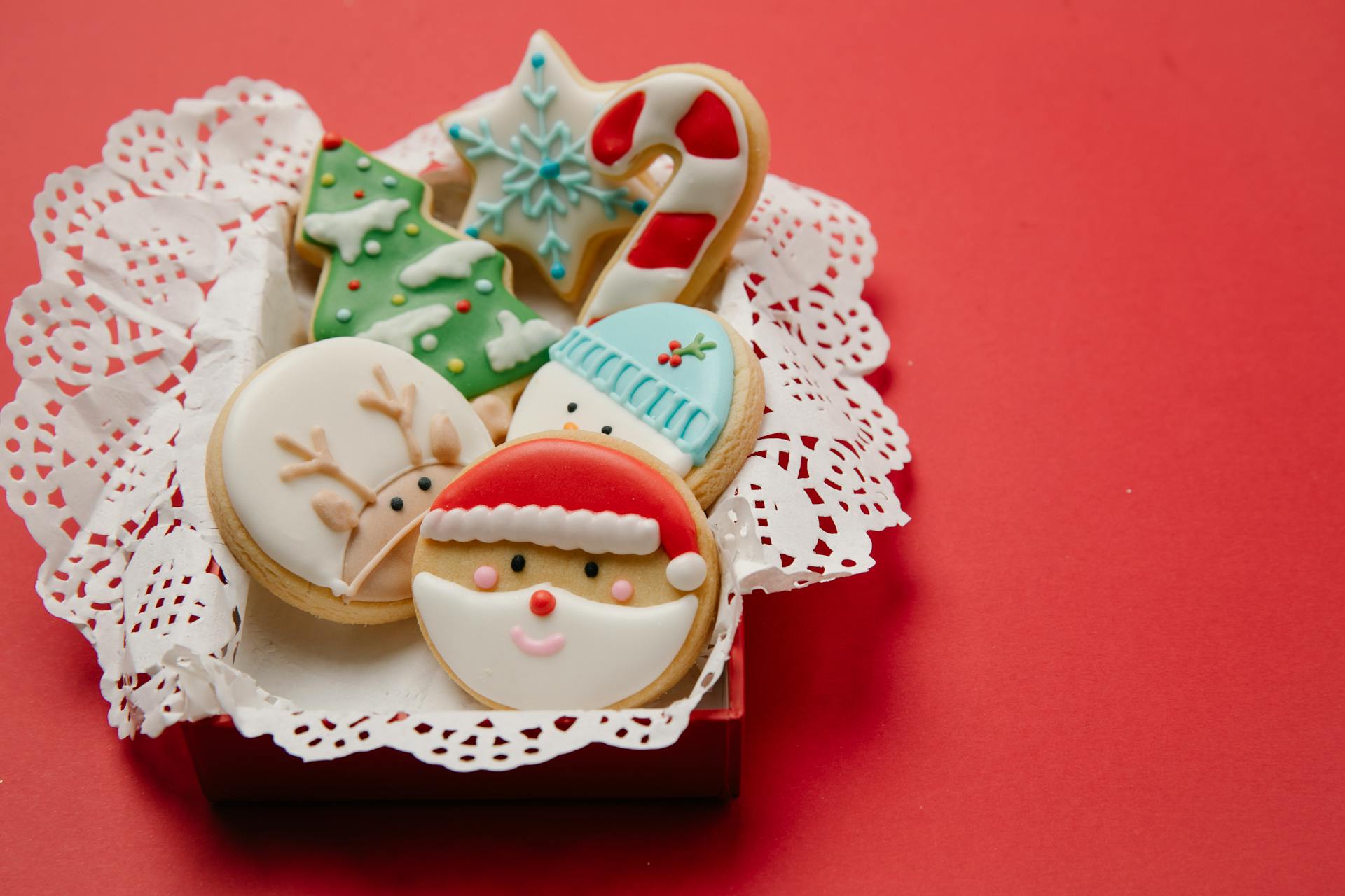 High angle of small box with Christmas biscuits decorated with colourful icing on white doily