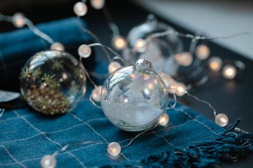 Transparent Christmas baubles filled with ornaments on table with blue warm scarf and glowing garland