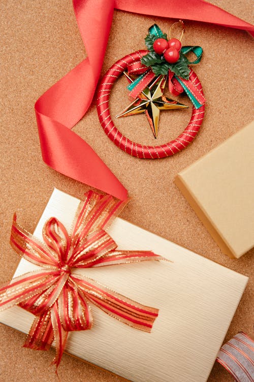 From above of Christmas gift box wrapped in golden paper and decorated with red ribbon and festive baubles on table