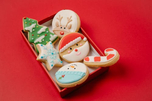 High angle of small box with traditional Christmas biscuits covered with colourful icing on red background