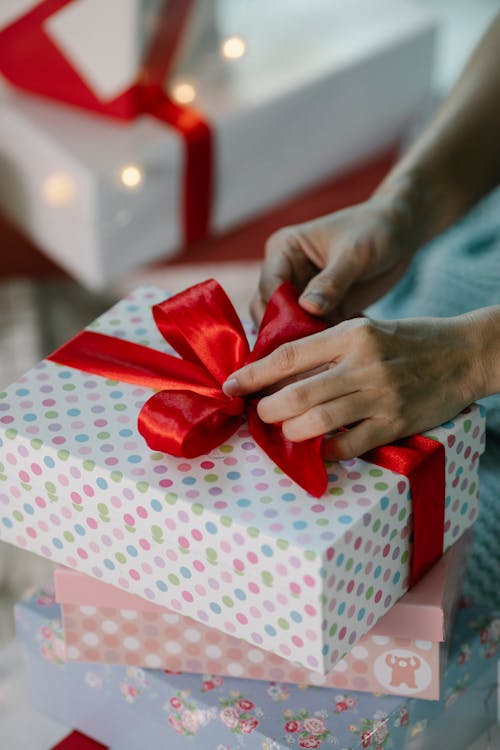 Unrecognizable woman tying red ribbon on wrapped box with present preparing for Christmas
