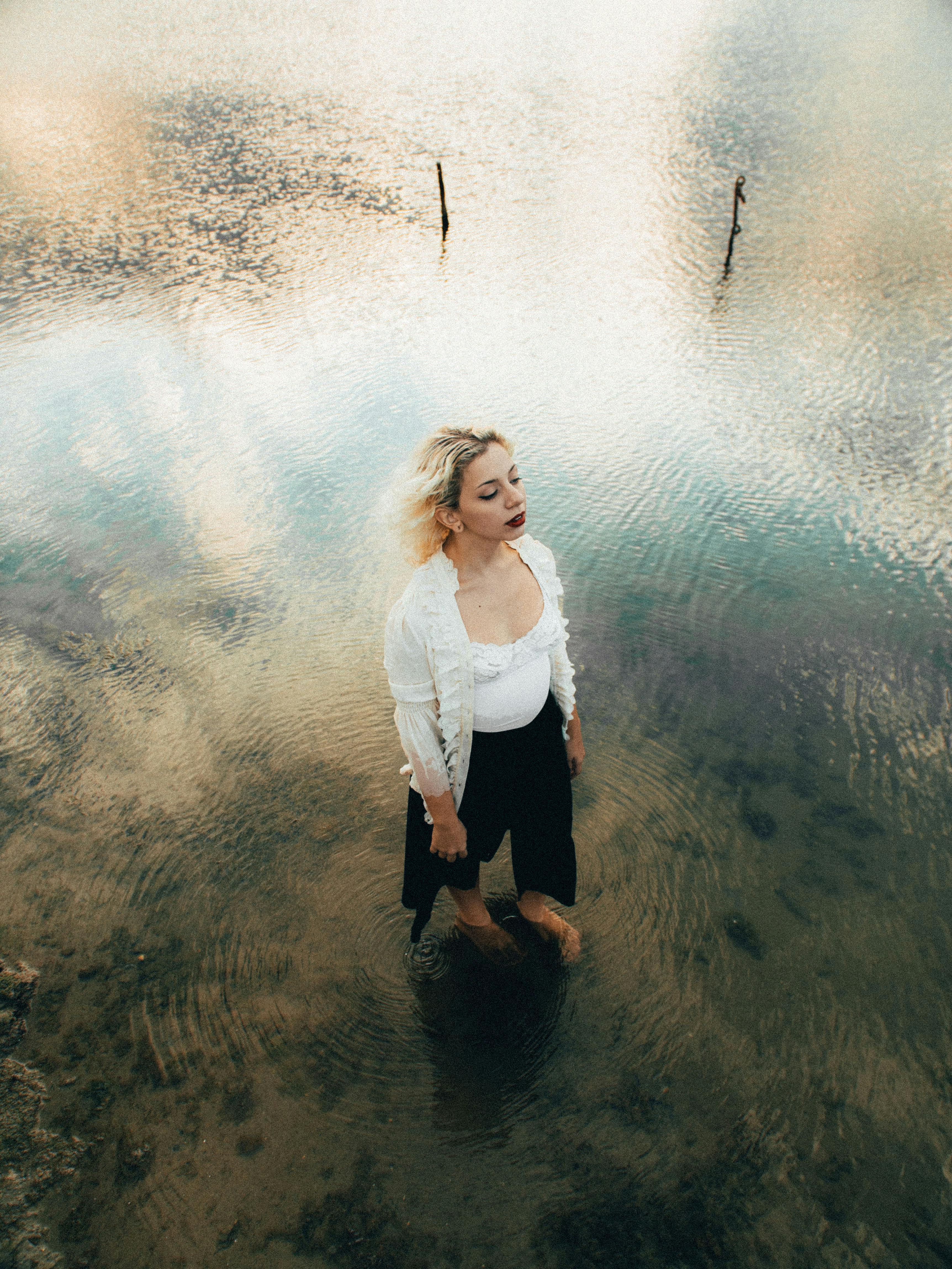 From above full length young attractive female in casual clothes standing in shallow lake water in peaceful park in daylight