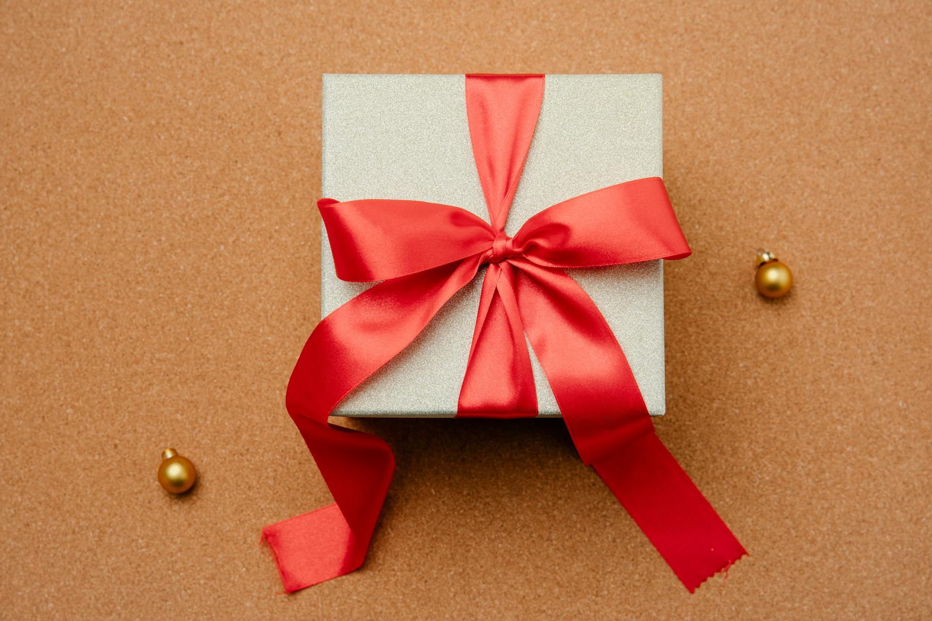Shiny gift box with red ribbon and golden baubles on brown backdrop. Perfect for celebrations.
