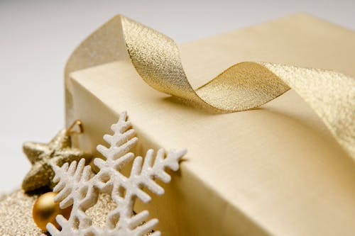 Closeup of golden wavy ribbon on wrapped box with Christmas present and festive baubles