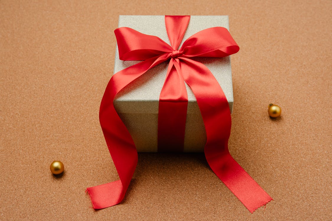Free High angle of small box with Christmas present decorated with red ribbon on table with festive baubles Stock Photo