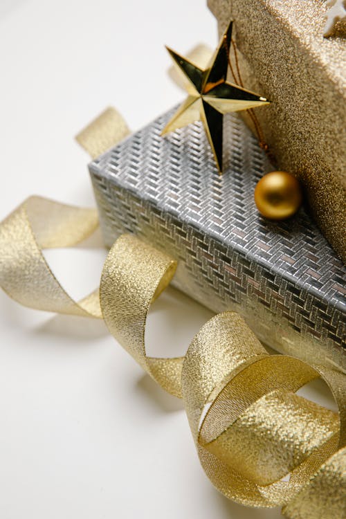 High angle of silver and golden Christmas gift boxes with wavy ribbon on grey background