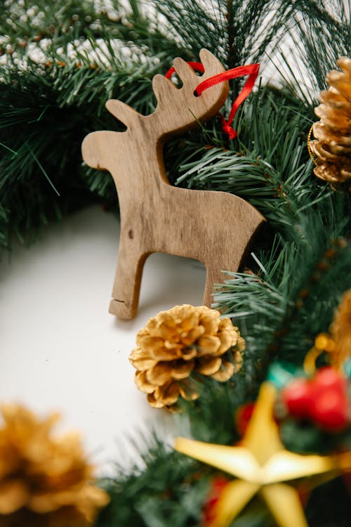 High angle of wooden reindeer toy near Christmas pine wreath and bumps with decorative elements placed on white surface