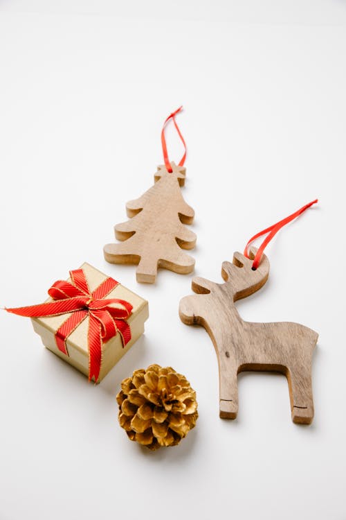 Top view of wooden toys in shape of reindeer and Christmas tree near small gift box and bump placed on white surface