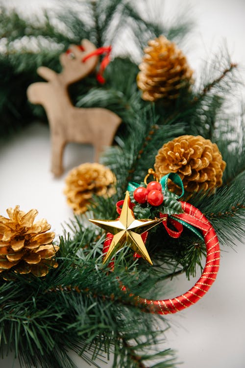 High angle of Christmas pine garland and cones with star and decorative objects near wooden reindeer toy placed on white background