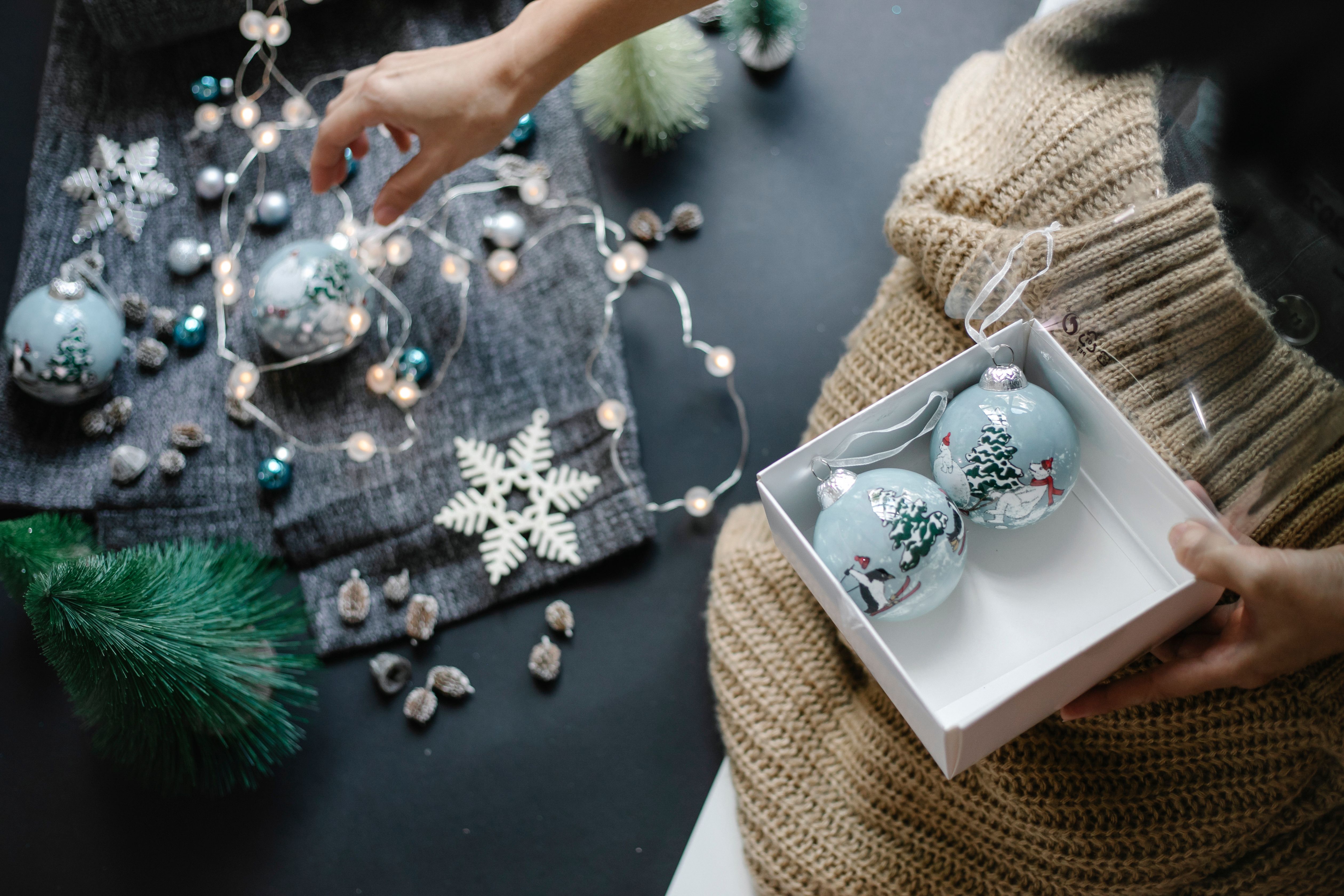 Hand arranging Christmas baubles amidst festive decor, setting a warm holiday atmosphere indoors.