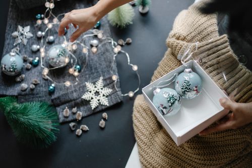 Free Crop unrecognizable female with Christmas balls in box decorating room with garland and baubles Stock Photo