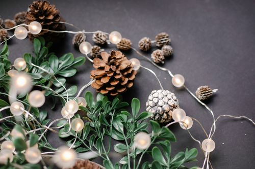 Free From above of glowing garland near pine cones and green leaves at home Stock Photo