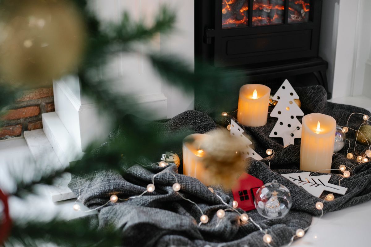 Candles and garland arranged beside a fireplace with a Christmas tree nearby