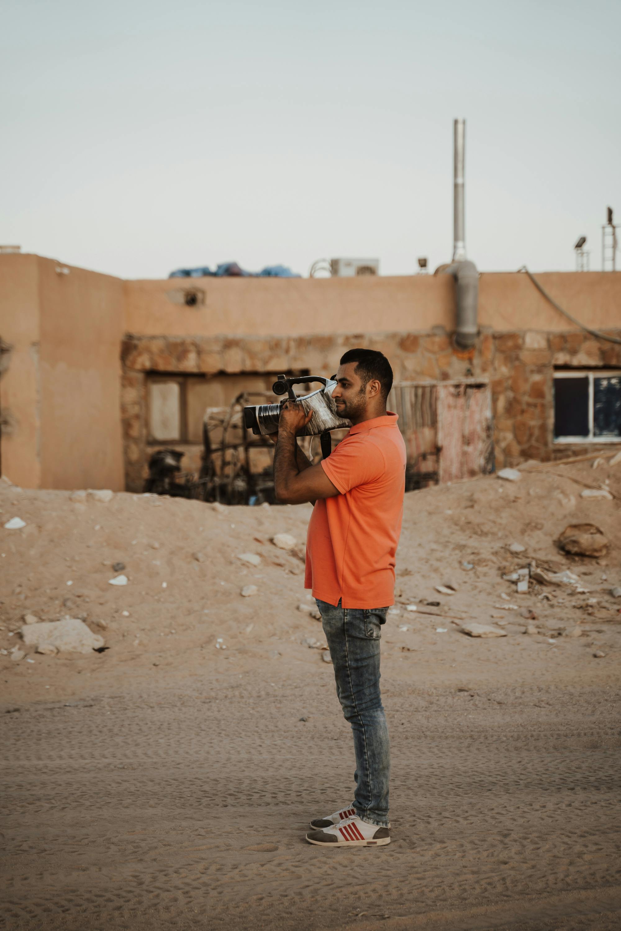 Side-view of a man holding a video camera in an Egyptian desert setting.