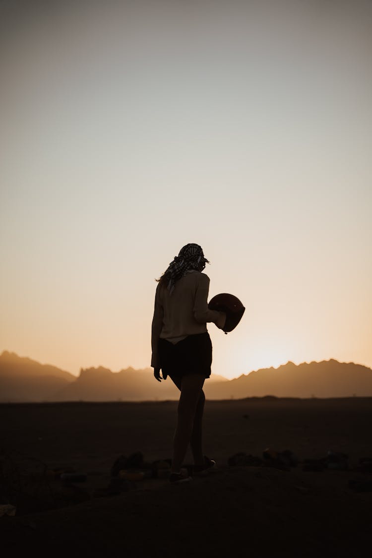 
A Silhouette Of A Woman Holding A Helmet