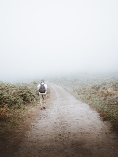 Unrecognizable backpacker walking on rural road on misty day