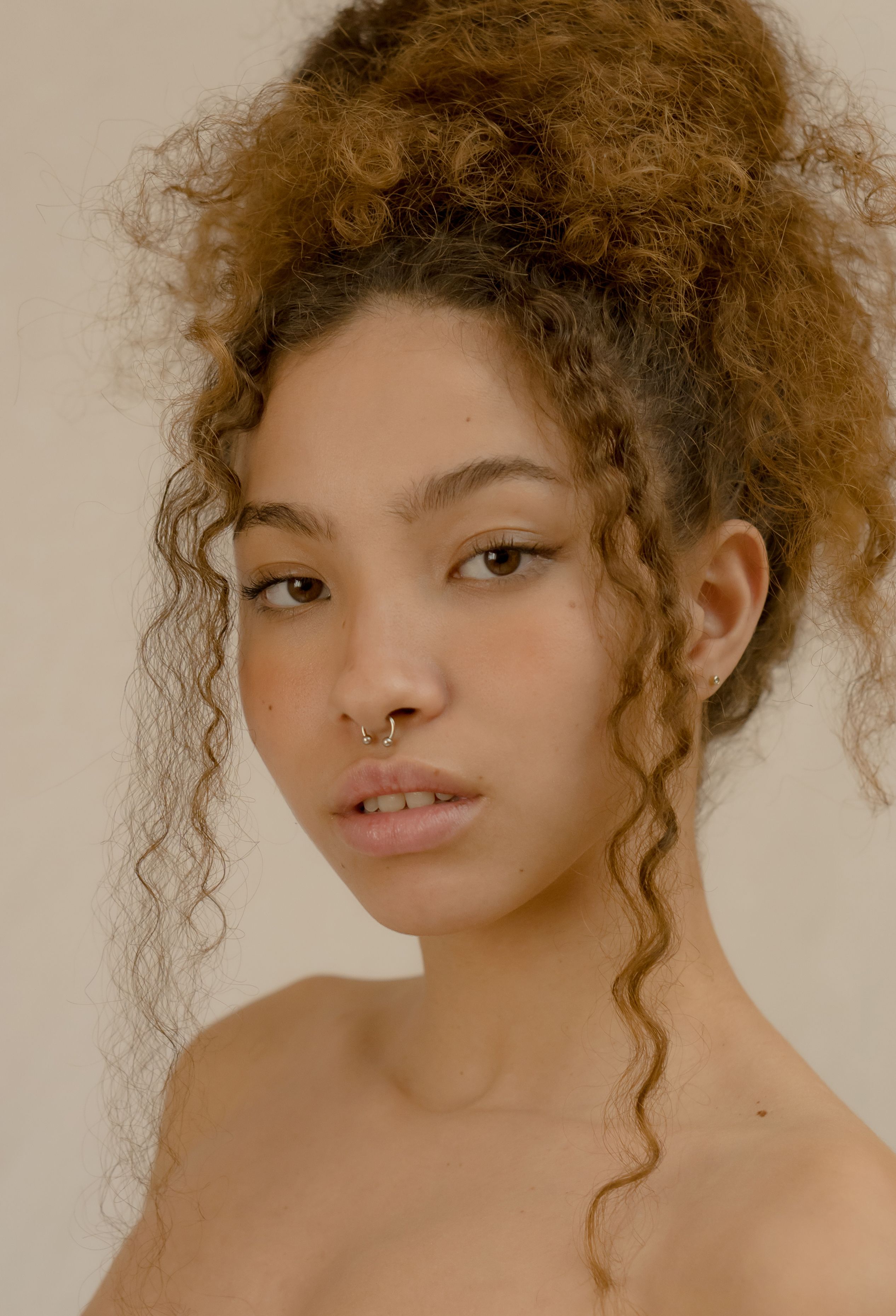 Captivating portrait of a woman with curly hair and nose piercing, exuding confidence and style.