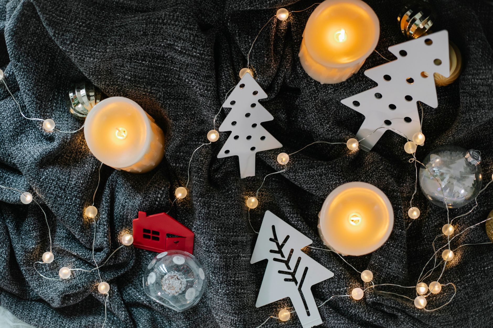 From above of burning candles and decorative toys in form of Christmas trees placed on gray fabric surface in daytime