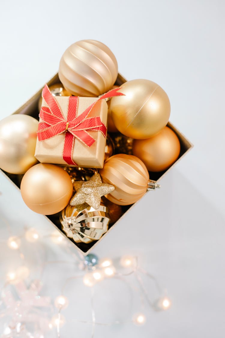 Box With Golden Baubles Placed On White Surface