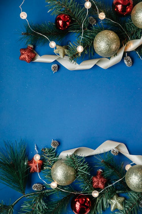 Top view of Christmas composition with decorative baubles and shiny garlands placed on green branches of fir against blue background