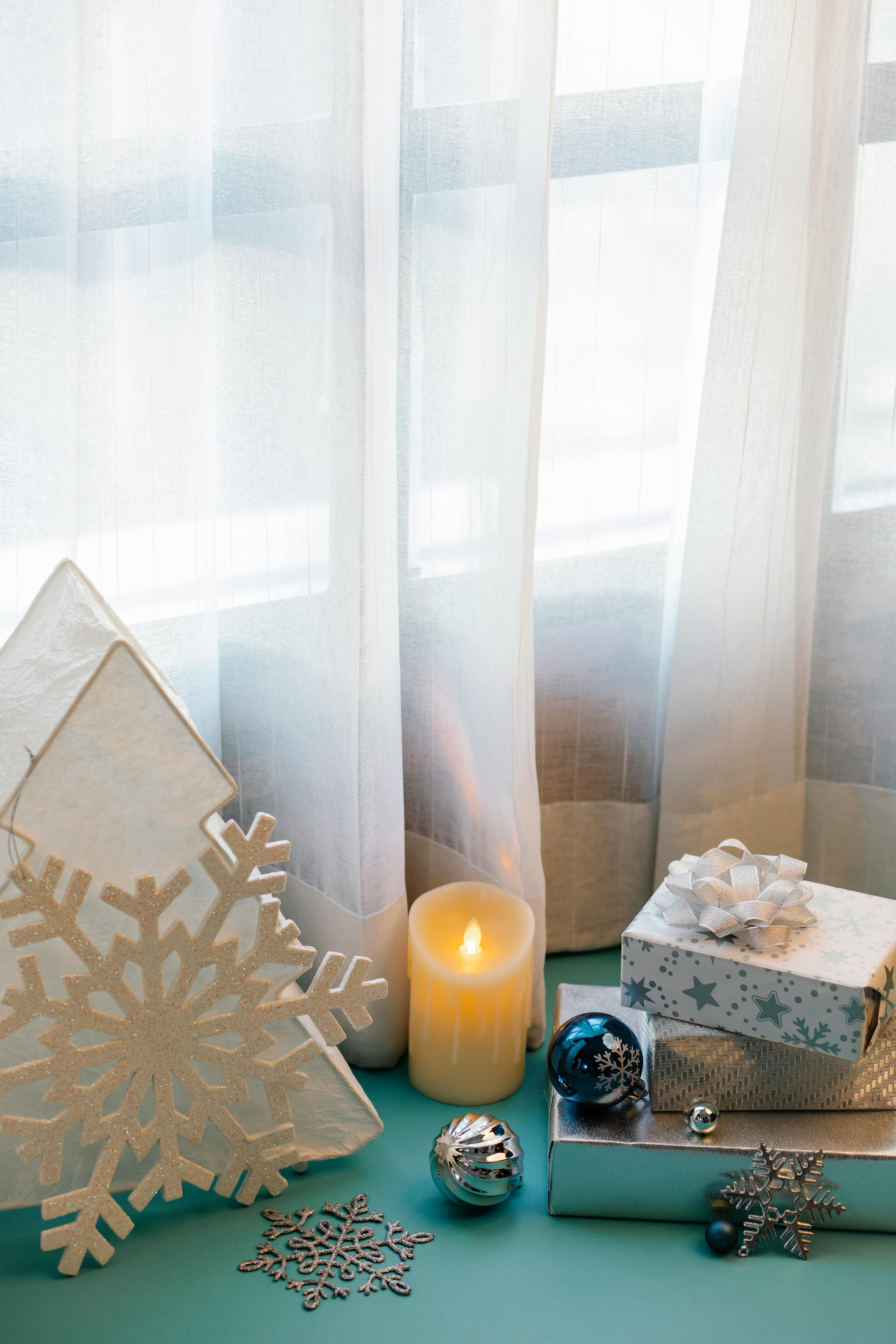 Christmas decorations and festive boxes with presents placed on blue surface near window with curtain in apartment