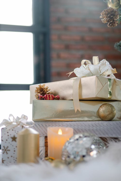 Pile of Christmas present boxes decorated with ribbons and bows and candles with baubles