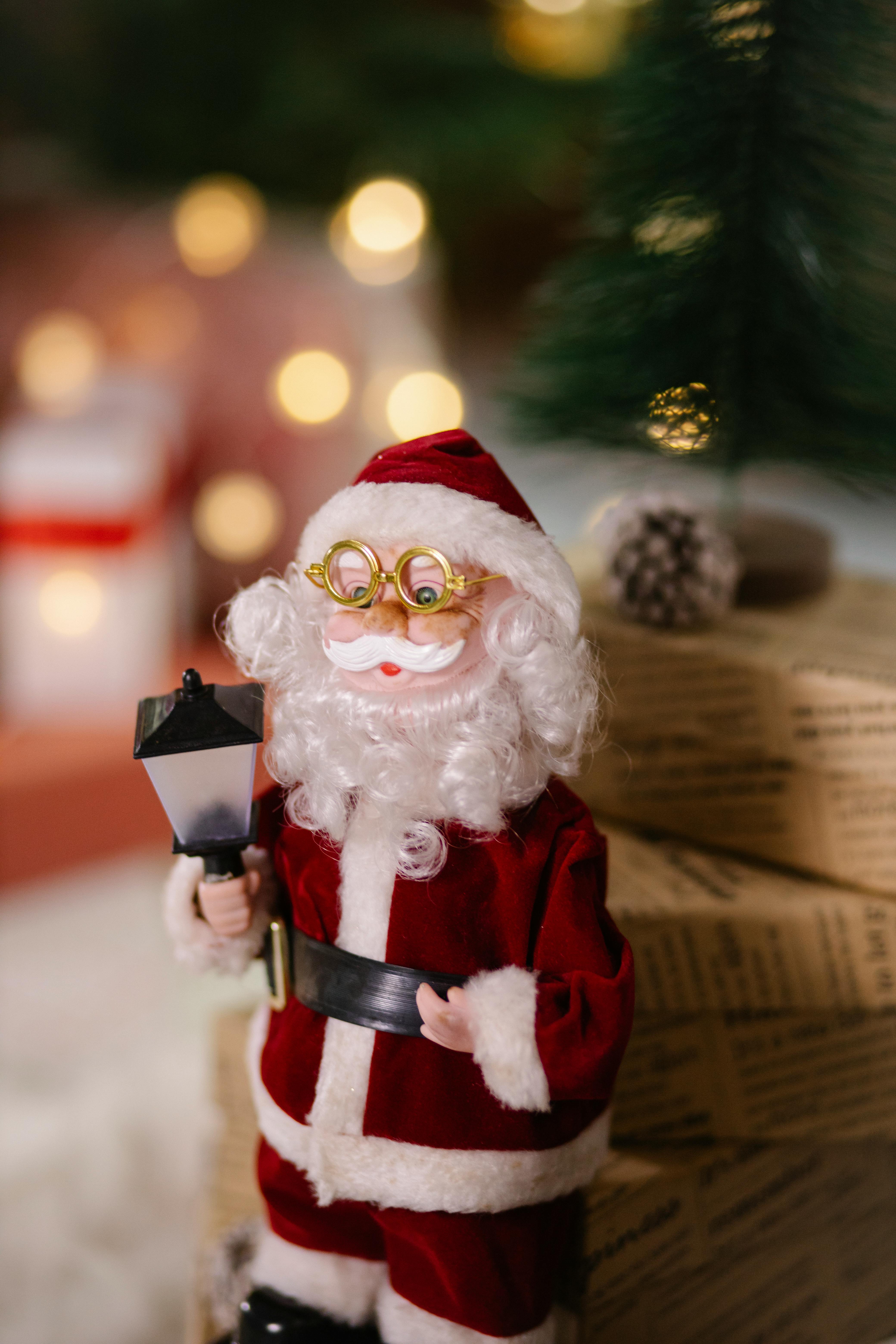 Small toy of Santa Claus in glasses placed near present boxes wrapped in decorative paper on blurred background