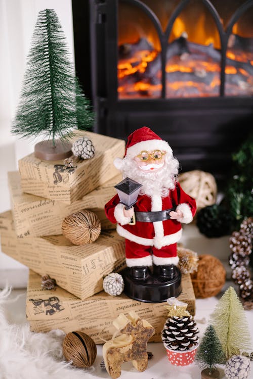 From above of Christmas wrapped present boxes and decorations with Santa Claus toy placed on floor near fireplace