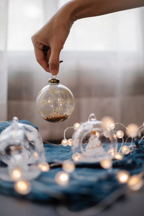 Free Crop unrecognizable female putting small glass ball with decorative filler on blue cloth with glowing fairy cloth Stock Photo