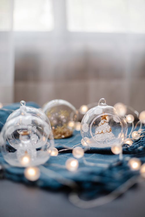 Collection of small decorative glass balls with figurines inside placed on blue cloth with glowing fairy lights