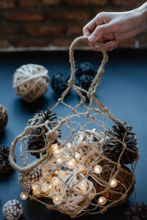 Crop anonymous person demonstrating bag with balls of threads and luminous garland with fir cones