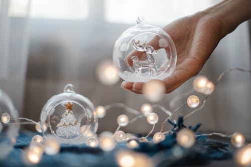 Crop anonymous person demonstrating decorative crystal ball under shining glowing garland prepared for Christmas