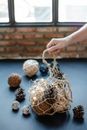 Crop anonymous person taking mash bag full of threads burning garland and fir cones for Christmas decoration