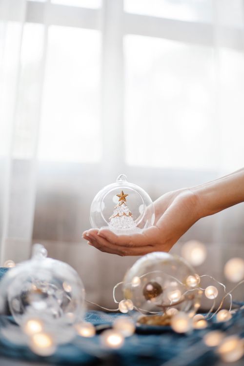 Free Crop anonymous person demonstrating crystal transparent ball on hand in room with shining garland during Christmas preparation Stock Photo