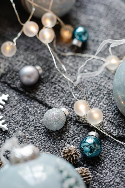From above of silver decorative Christmas balls and shiny garland placed near fir cones on plaid
