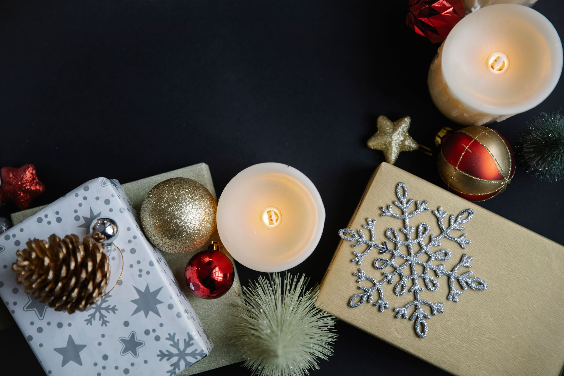 Top view of different Christmas decorations with snowflake on gift boxes near balls and candles with stars near fake small spruce on black background