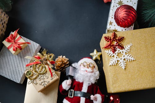 Top view composition of various colorful bright Christmas present boxes wrapped in decorative paper and toy of Santa Claus on black background