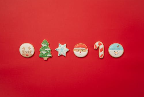 Top view of assorted Christmas cookies of different shapes decorated with colorful icing and arranged in row on red background