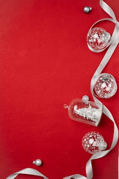 From above of assorted creative Christmas tree glass baubles placed on red surface with silver ribbon