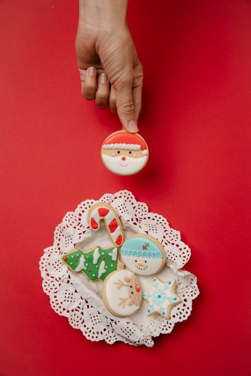 Top view of crop anonymous female demonstrating delicious homemade gingerbread Christmas cookies decorated with colorful icing and served on red background