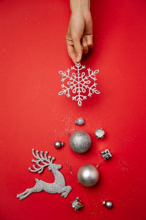 Top view of crop faceless lady decorating red surface with silver snowflake and various shiny baubles