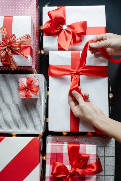 Top view of crop unrecognizable person tying red band on present box while preparing for New Year holiday