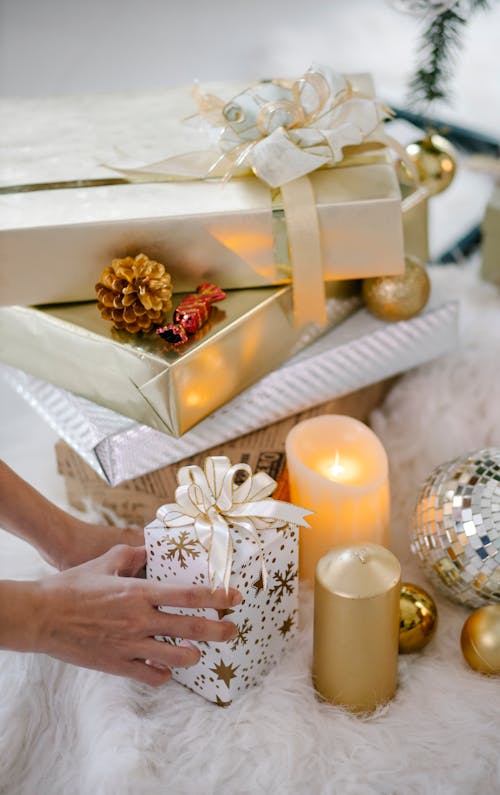 High angle of crop unrecognizable person with assorted present boxes and decorative candles on soft textile on Christmas day