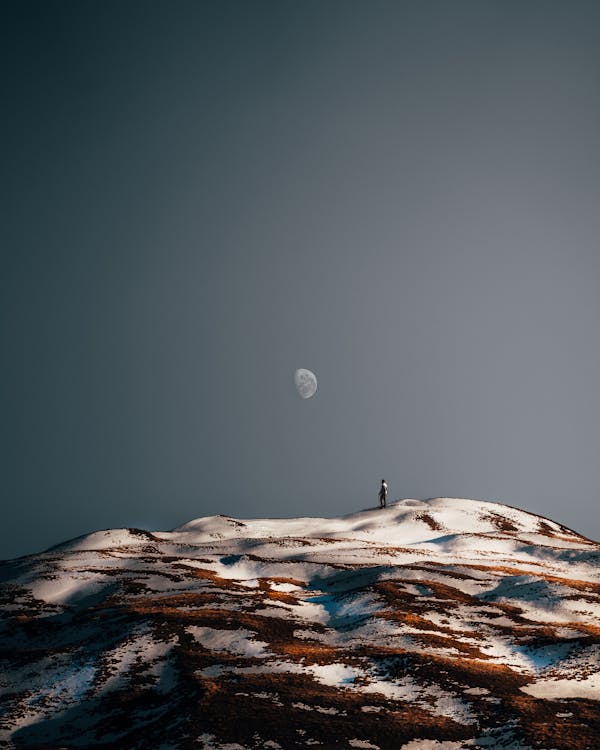 Photo of a Person Standing on a Hill with Snow